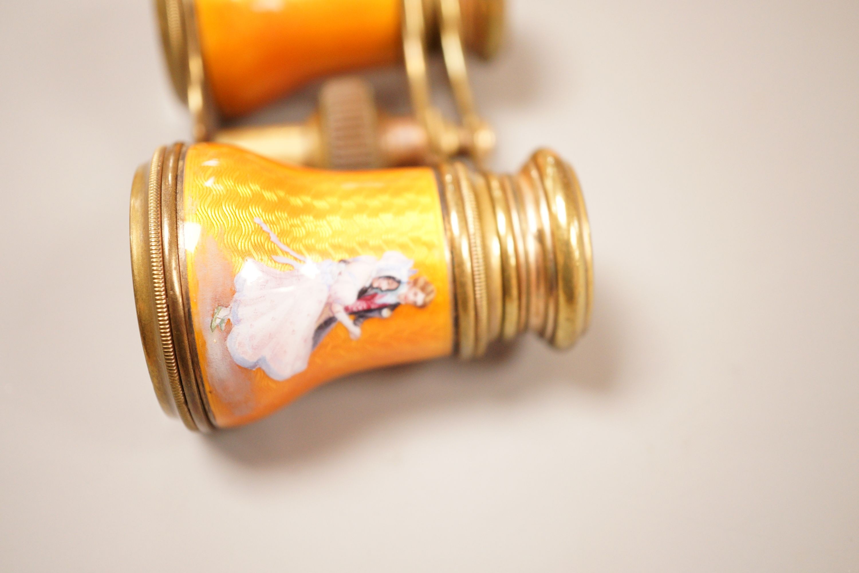 A pair of German orange enamelled opera glasses, inscribed Fabr Emil Busch, Rathenow to the left lens, and E. Petitpierre, BerlinFriedrichstr. to the right lens, 10cm wide